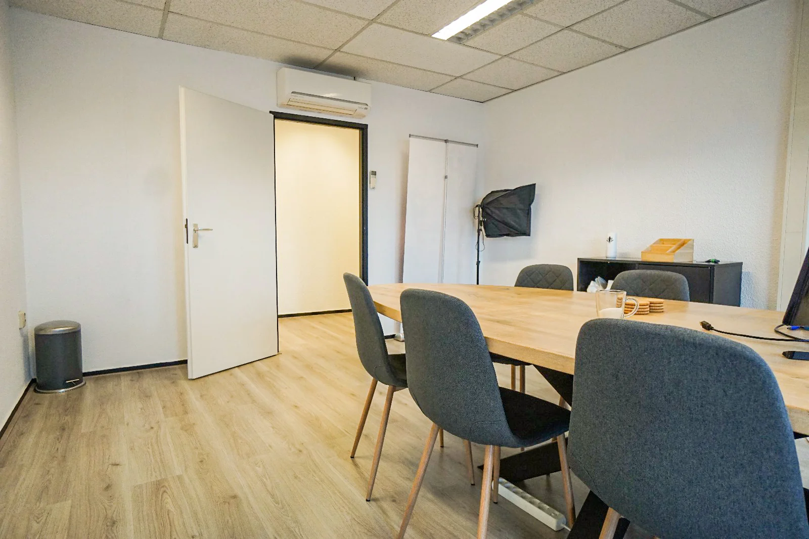 Vergaderruimte aan de Hollantlaan met houten tafel, grijze stoelen en studiolamp in de hoek.