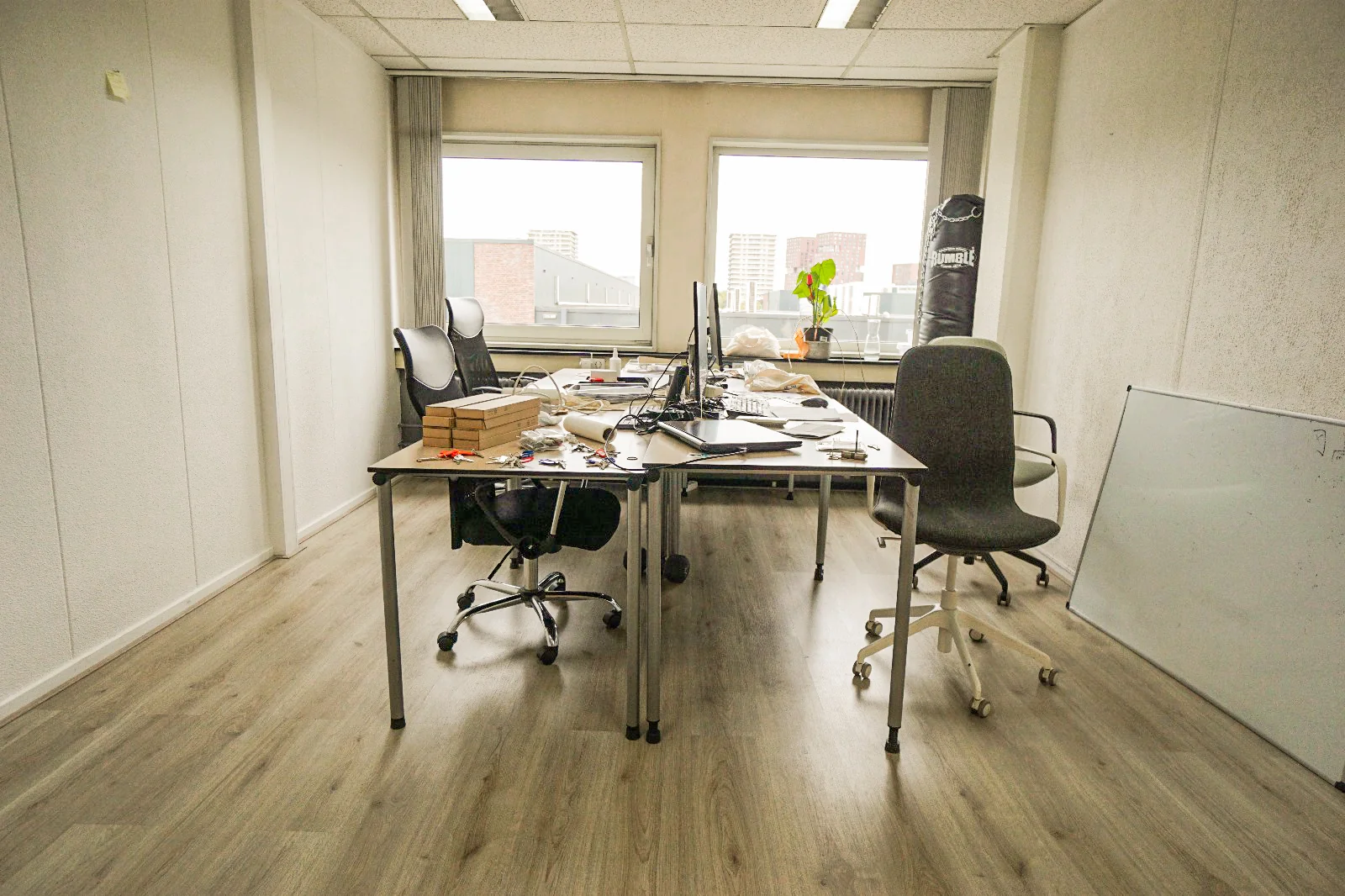 Kantoorkamer aan de Hollantlaan met twee bureaus, stoelen, computerschermen en een bokszak in de hoek.