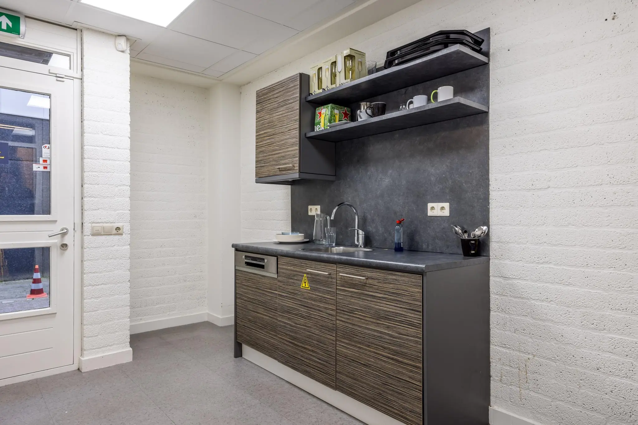 Moderne pantry met houten keukenkastjes, grijs aanrechtblad en open wandplanken in een kantoor aan de Atoomweg.