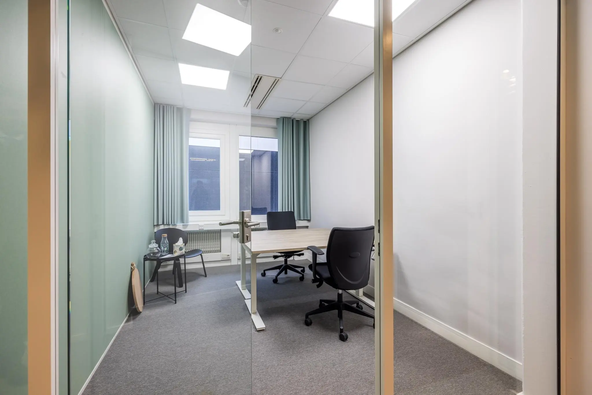 Kleine, moderne kantoorruimte aan de Atoomweg met twee bureaustoelen, een bureau en een zithoek bij het raam.