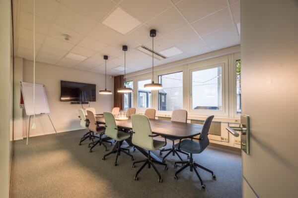 Vergaderkamer aan de Atoomweg met lange tafel, moderne stoelen, whiteboard en flatscreen.