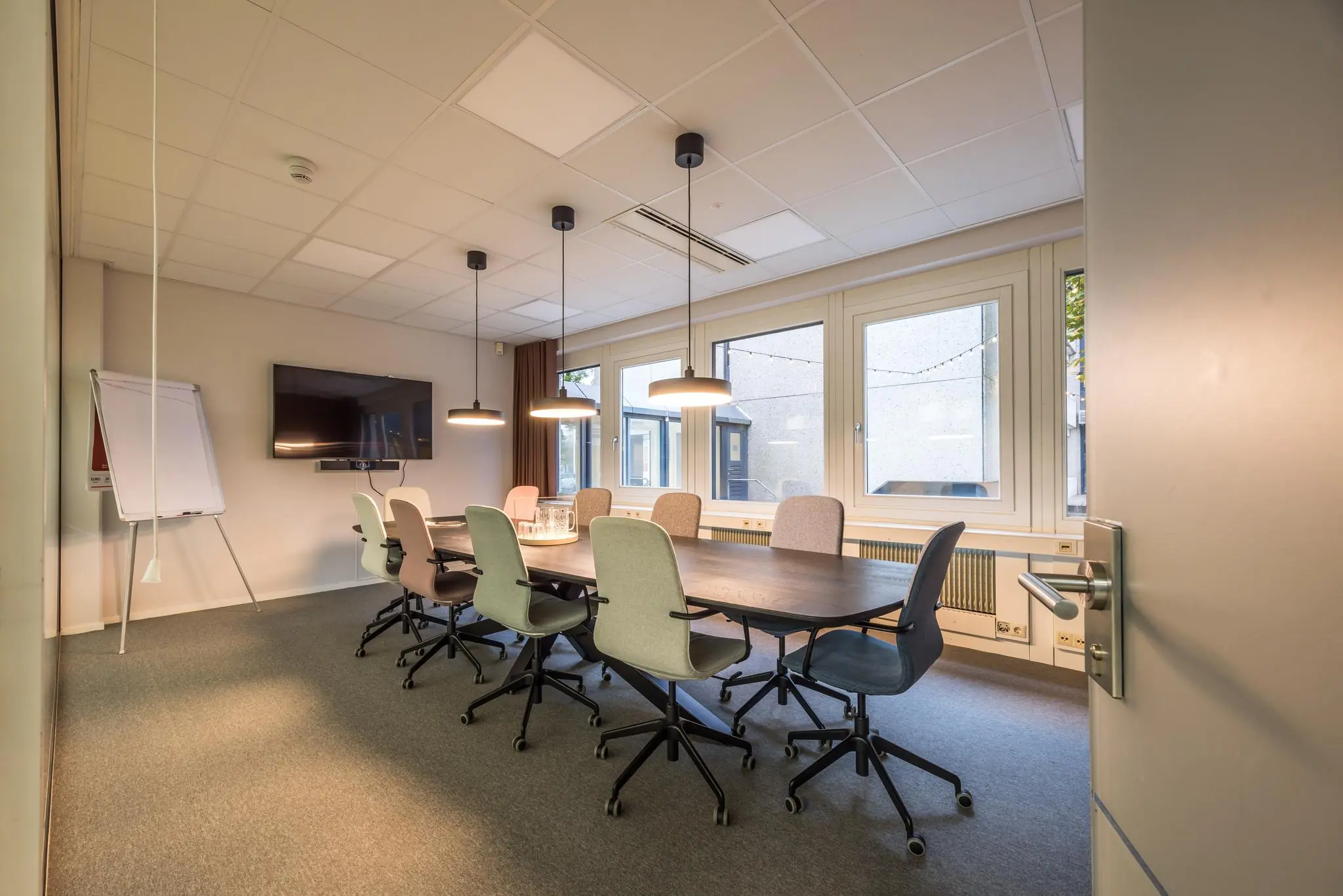 Vergaderkamer aan de Atoomweg met lange tafel, moderne stoelen, whiteboard en flatscreen.