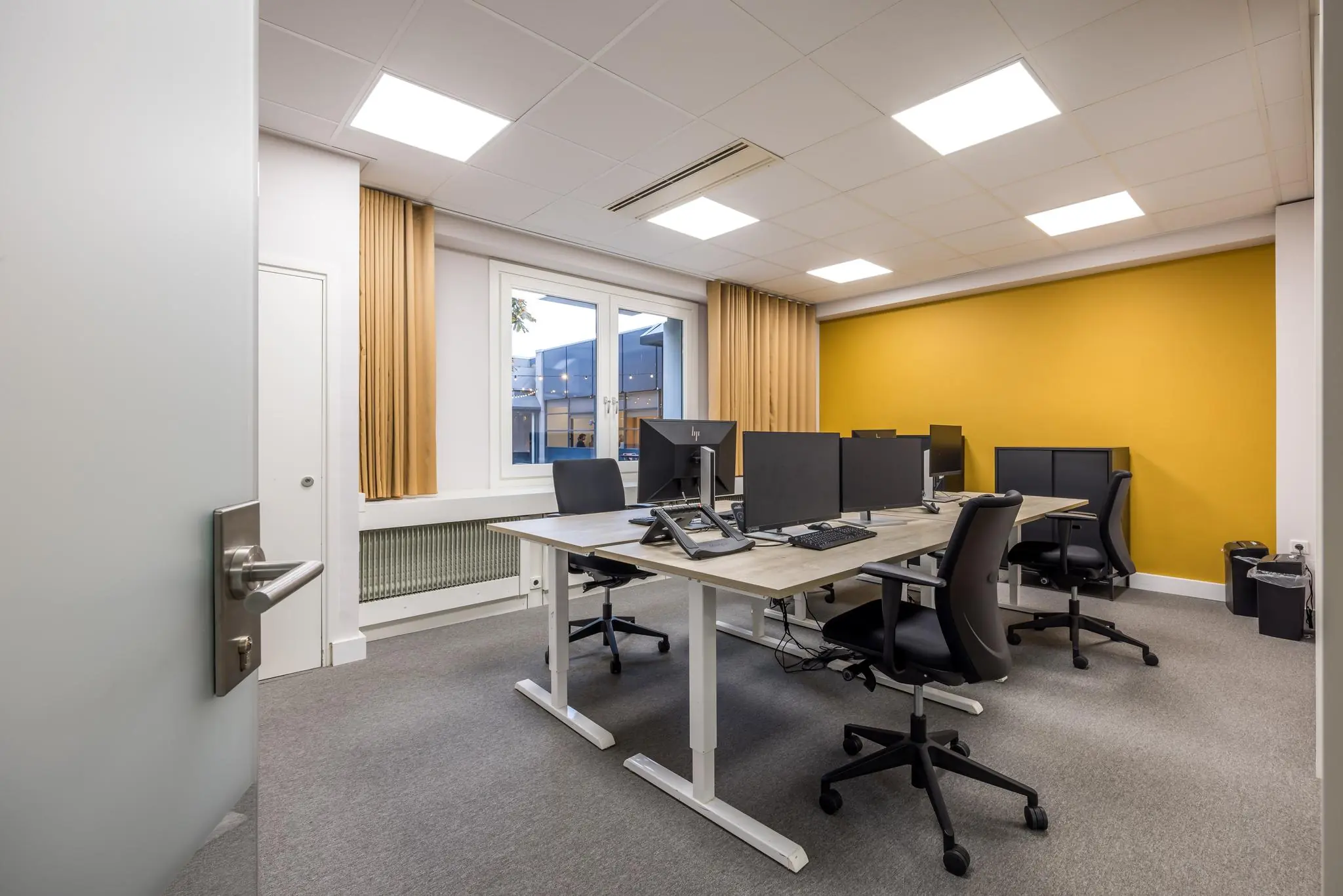 Moderne kantoorruimte aan de Atoomweg met werkplekken, bureaustoelen en een opvallende gele accentmuur.