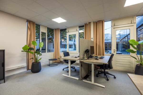 Modern kantoor met twee werkplekken, grote ramen, beige gordijnen en groene kamerplanten aan de Atoomweg.