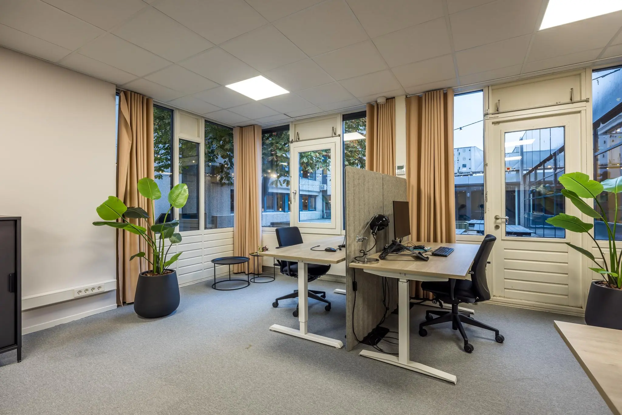 Modern kantoor met twee werkplekken, grote ramen, beige gordijnen en groene kamerplanten aan de Atoomweg.