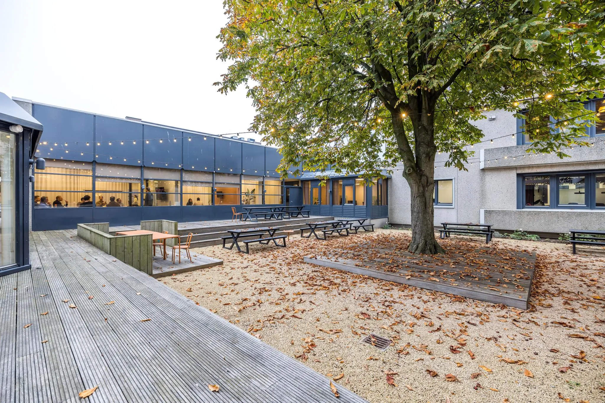Binnenplein van een modern kantoorgebouw aan de Atoomweg met zitbanken, herfstbladeren en sfeerverlichting.