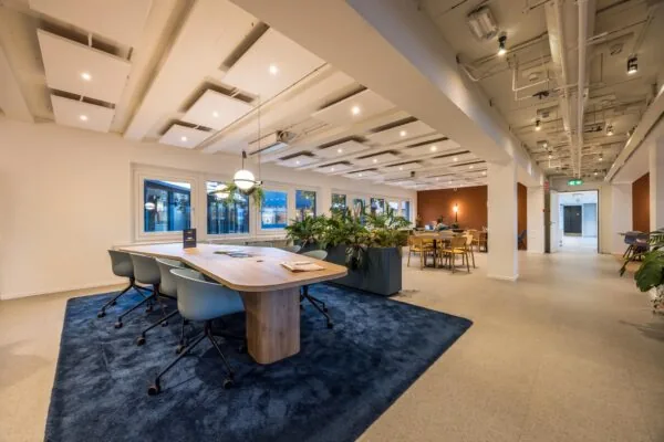 Modern ingericht kantoorinterieur aan de Atoomweg met houten tafels, designstoelen, planten en sfeervolle verlichting.