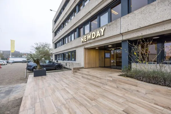 De hoofdingang van het kantoorgebouw aan de Atoomweg met het verlichte logo van NEWDAY boven de entree.