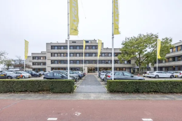 Kantoorpand van NewDay aan de Atoomweg met parkeerterrein en vlaggenmast op de voorgrond.