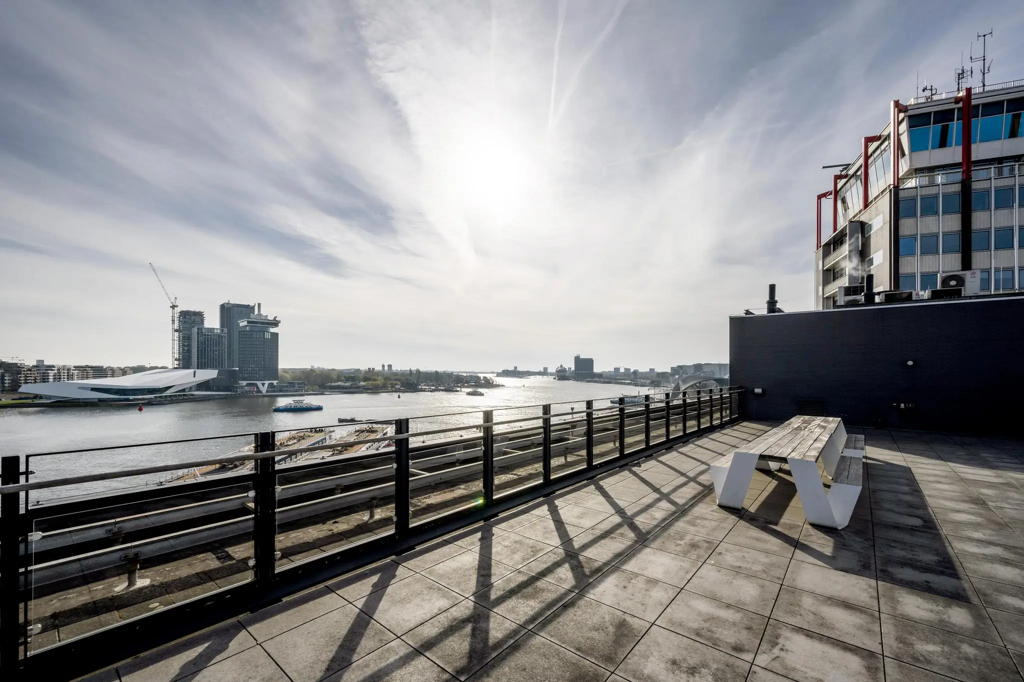 Zonovergoten dakterras aan de De Ruijterkade met uitzicht op het IJ en de skyline van Amsterdam.
