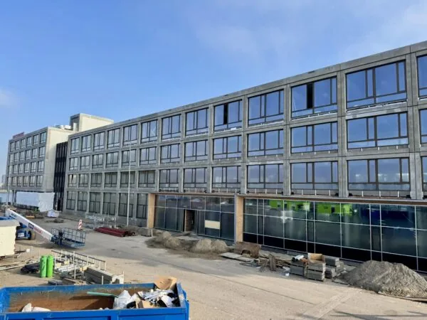 Groot modern gebouw aan de Sluisjesdijk in aanbouw, met glazen gevel en bouwmaterialen op de voorgrond.