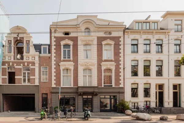 Voorgevel van klassieke herenhuizen aan de Plantage Middenlaan in Amsterdam met geparkeerde fietsen en scooters op de stoep.