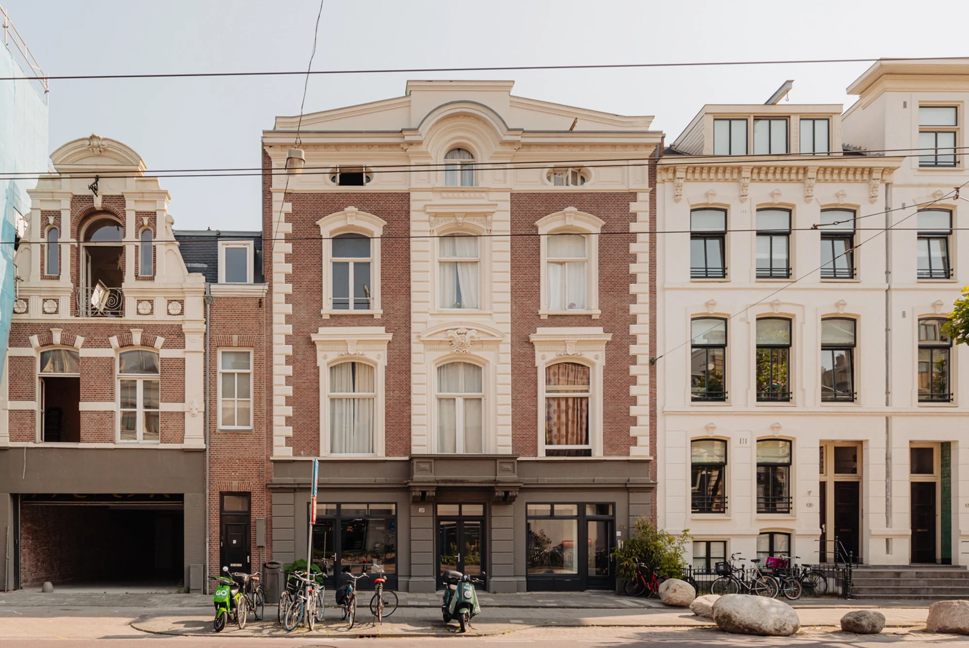 Voorgevel van klassieke herenhuizen aan de Plantage Middenlaan in Amsterdam met geparkeerde fietsen en scooters op de stoep.