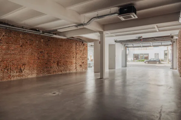 Lichte, industriële ruimte met betonnen vloer, bakstenen muur en een open garagedeur aan de Plantage Middenlaan.