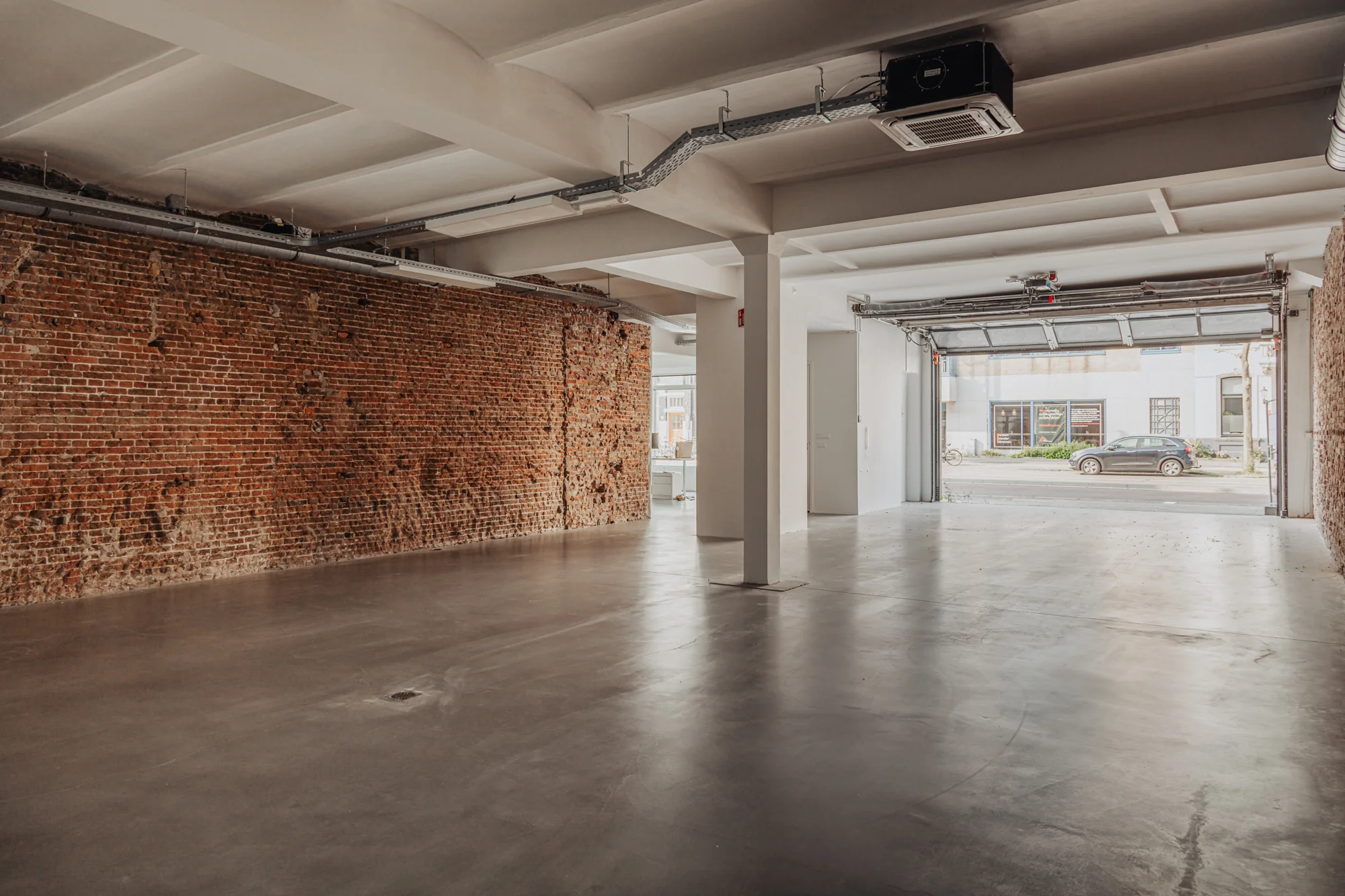 Lichte, industriële ruimte met betonnen vloer, bakstenen muur en een open garagedeur aan de Plantage Middenlaan.