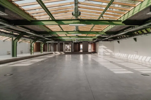 Lichte industriële ruimte met groene stalen balken, betonnen vloer en een dak van glas aan de Plantage Middenlaan.