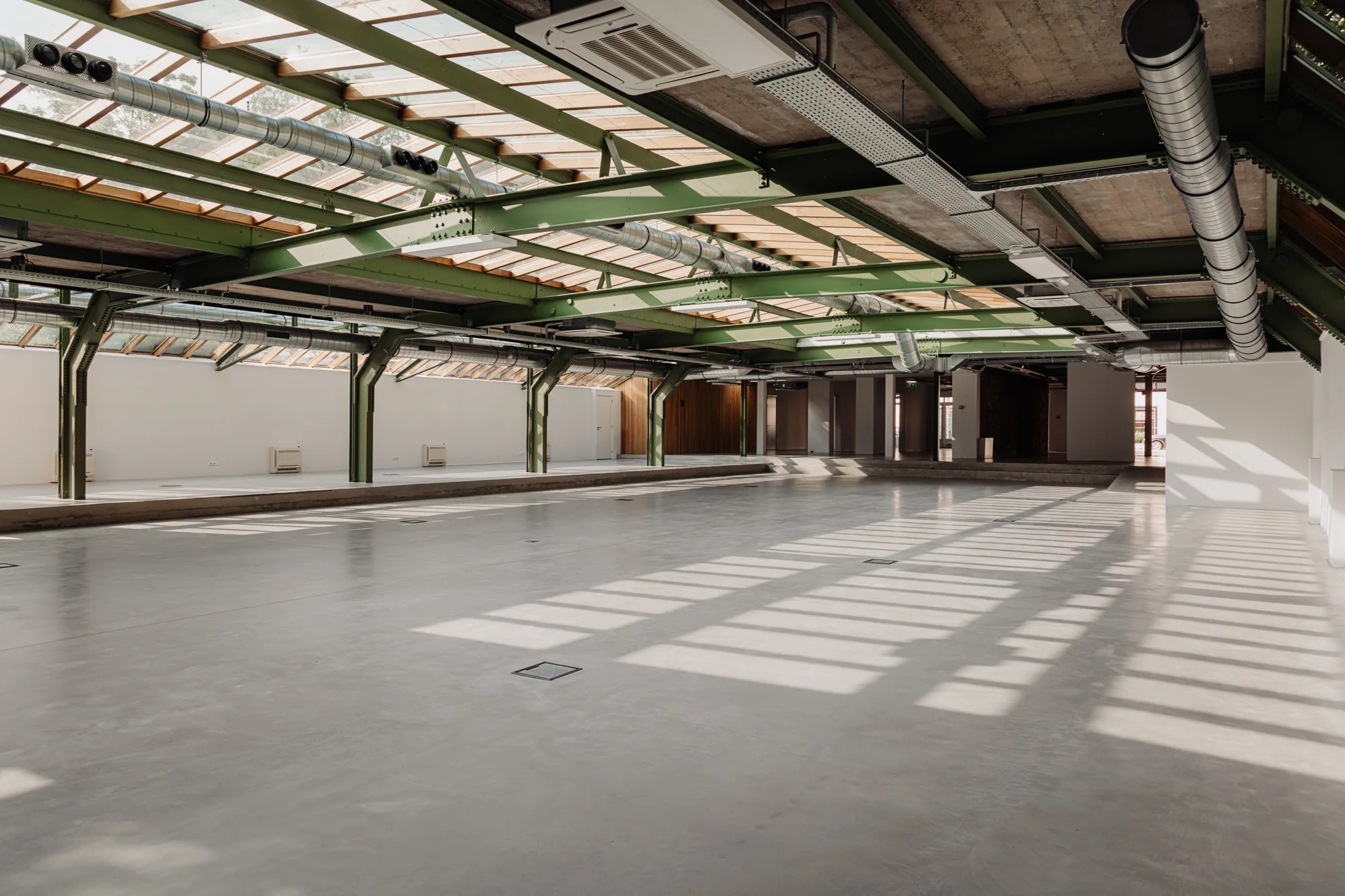 Lichte, industriële ruimte met groene stalen draagconstructie en glazen dak aan de Plantage Middenlaan.