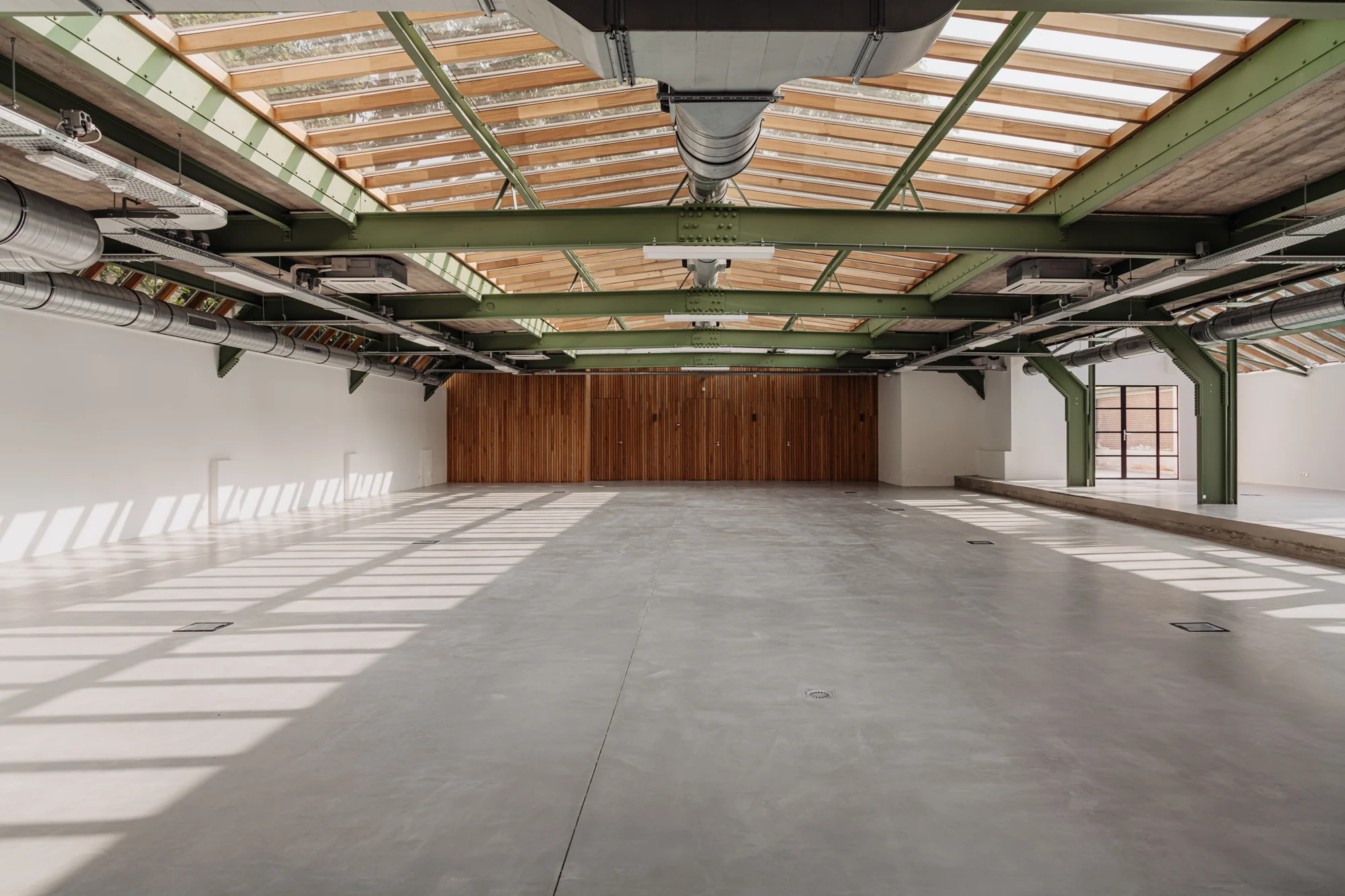 Licht en ruim industrieel interieur met betonnen vloer, groene staalconstructie en houten wand aan de Plantage Middenlaan.