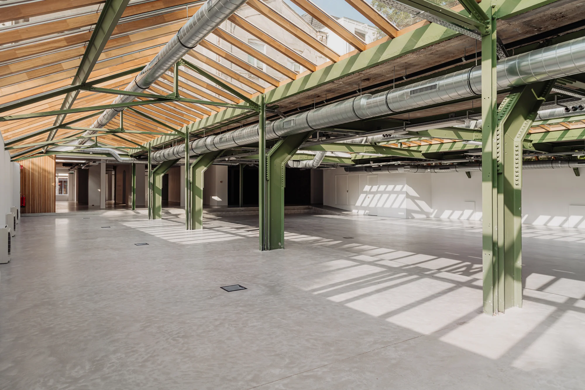 Lichte, industriële binnenruimte aan de Plantage Middenlaan met groene stalen balken, glazen dak en zichtbare ventilatiebuizen.