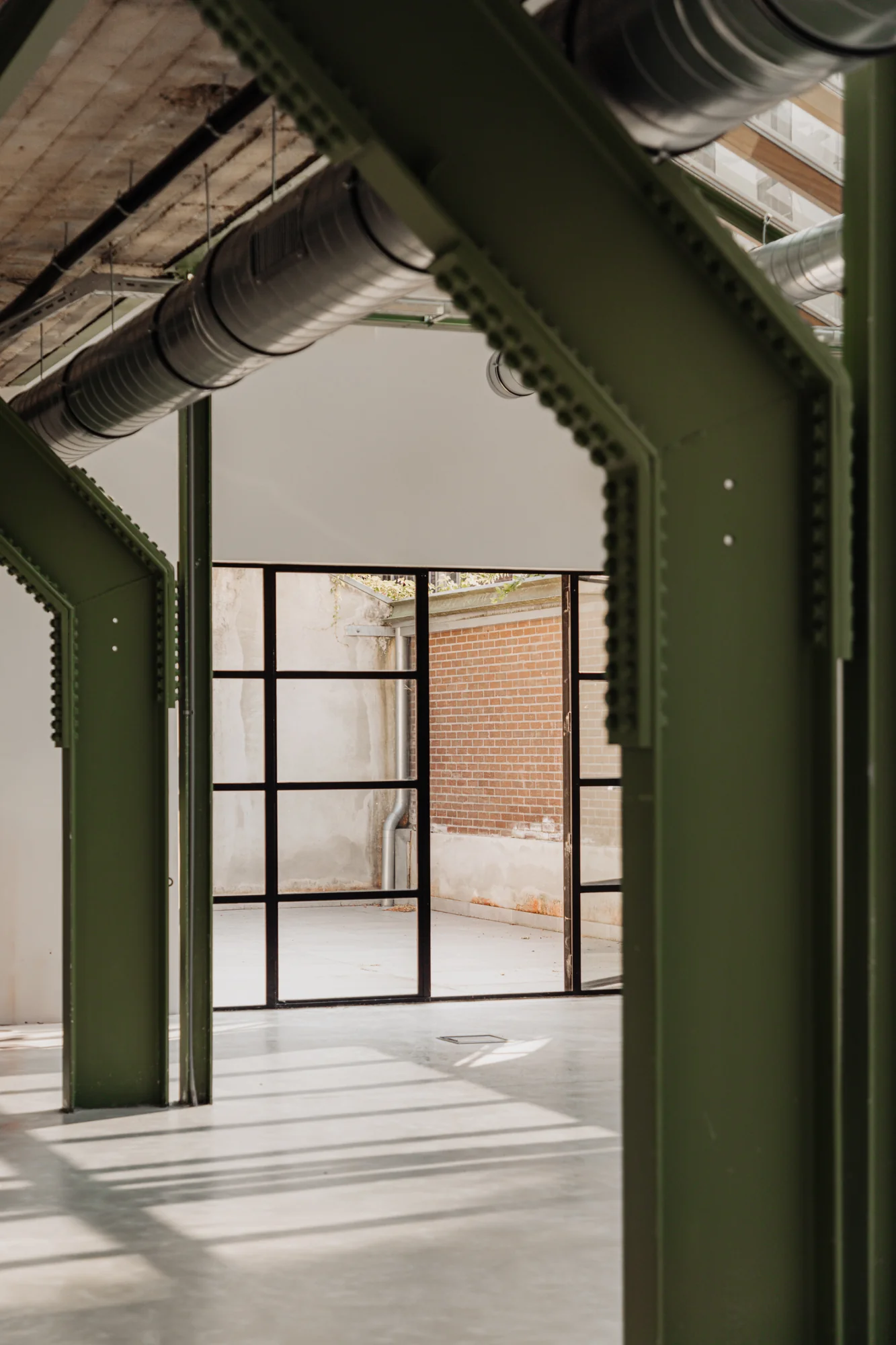 Industriële ruimte aan de Plantage Middenlaan met groene stalen balken, zicht op glazen deuren en een binnenplaats met bakstenen muur.