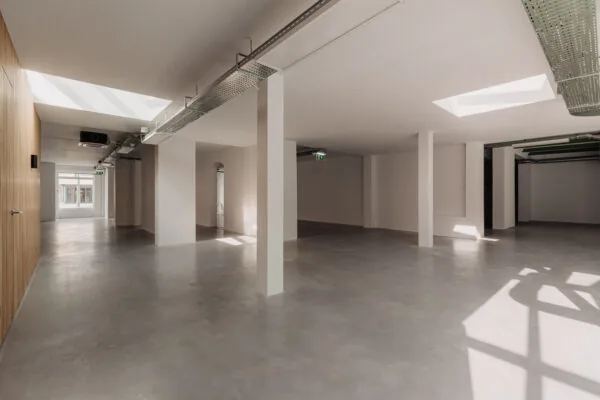 Licht en modern interieur van een leegstaand pand aan de Plantage Middenlaan met betonnen vloer, witte muren en zichtbare plafondinstallaties.