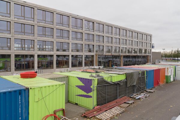 Bouwplaats aan de Sluisjesdijk met kleurrijke containers en een modern kantoorgebouw in aanbouw.