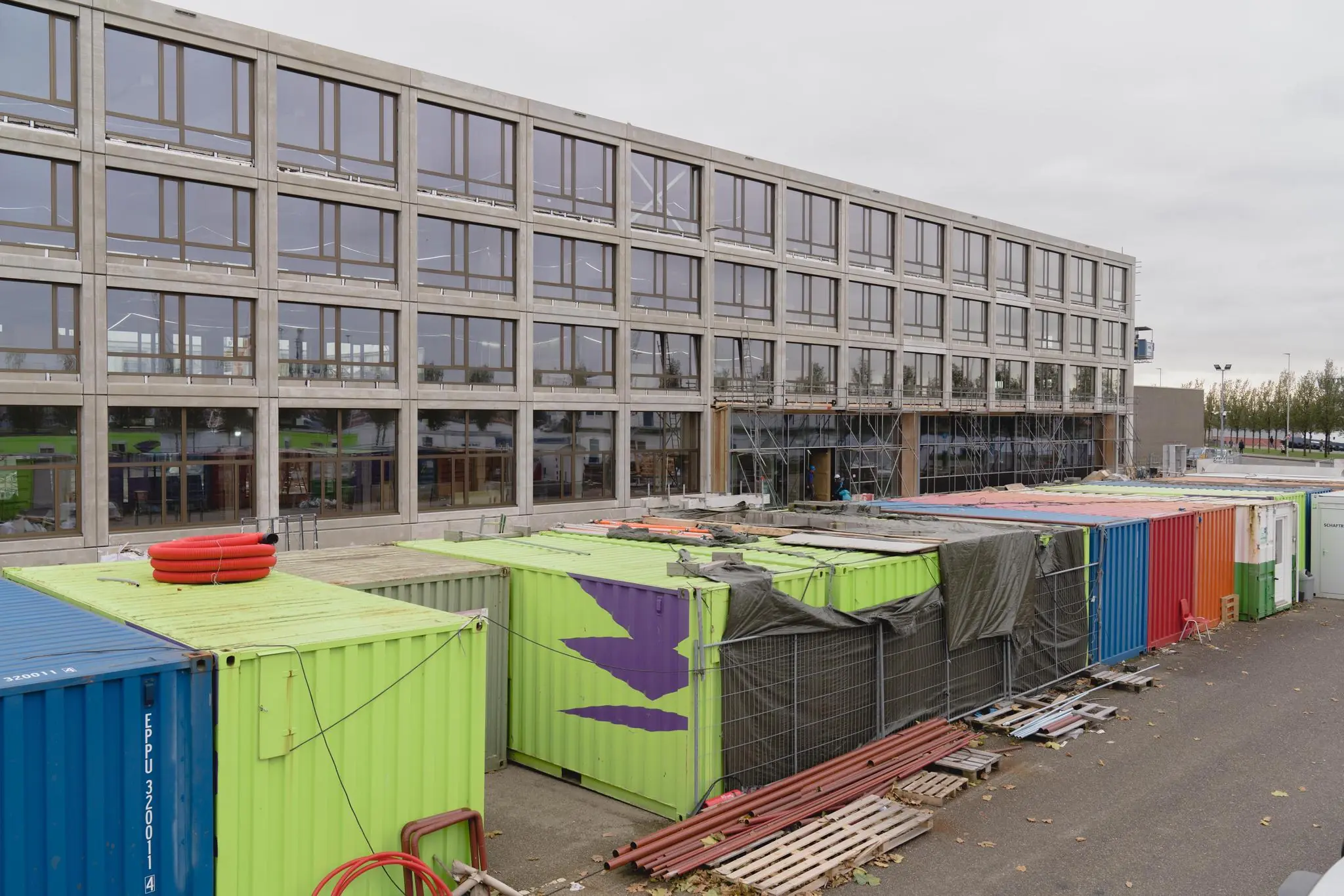 Bouwplaats aan de Sluisjesdijk met kleurrijke containers en een modern kantoorgebouw in aanbouw.
