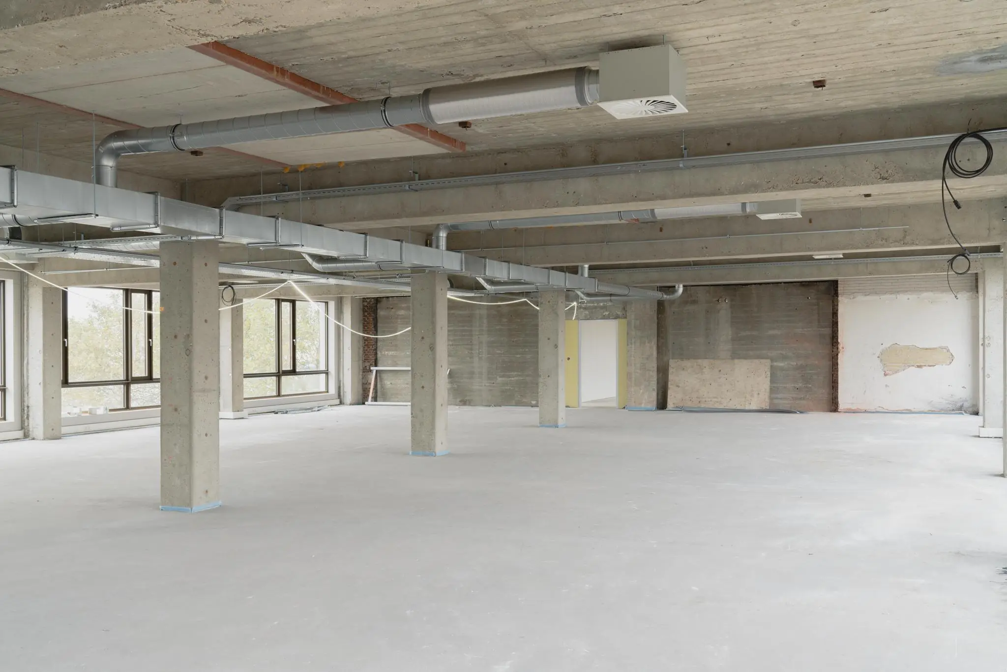 Leegstaande verdieping aan de Sluisjesdijk met betonnen pilaren, zichtbare ventilatiebuizen en grote ramen.