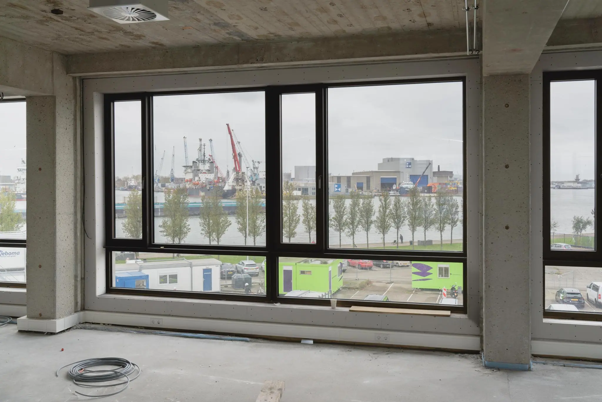 Uitzicht vanuit een casco kantoorpand aan de Sluisjesdijk op een industriegebied met scheepskranen en de kade aan de overkant van het water.