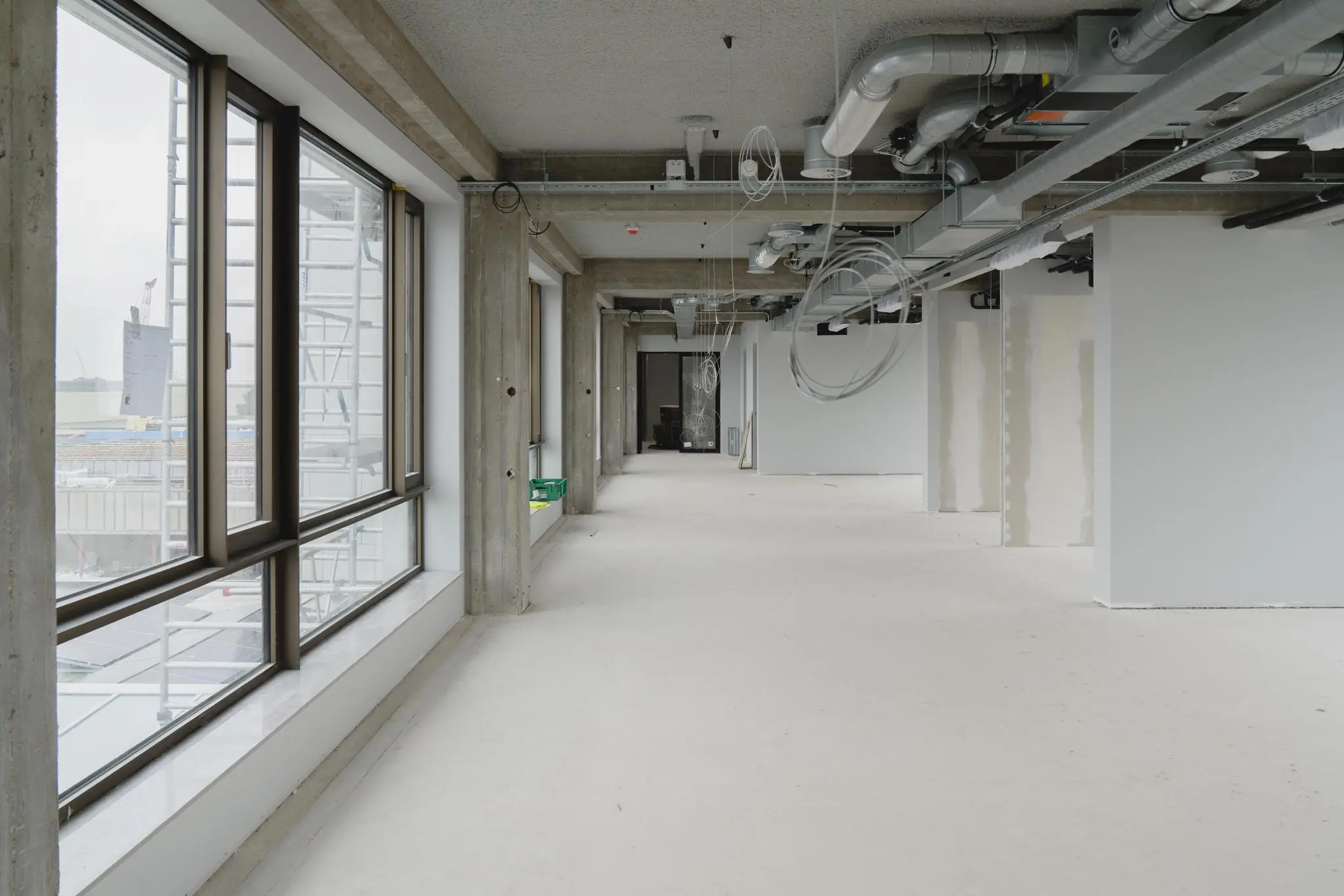 Leeg kantoorpand aan de Sluisjesdijk in verbouwing met zicht op onafgewerkte plafonds, leidingen en grote ramen.