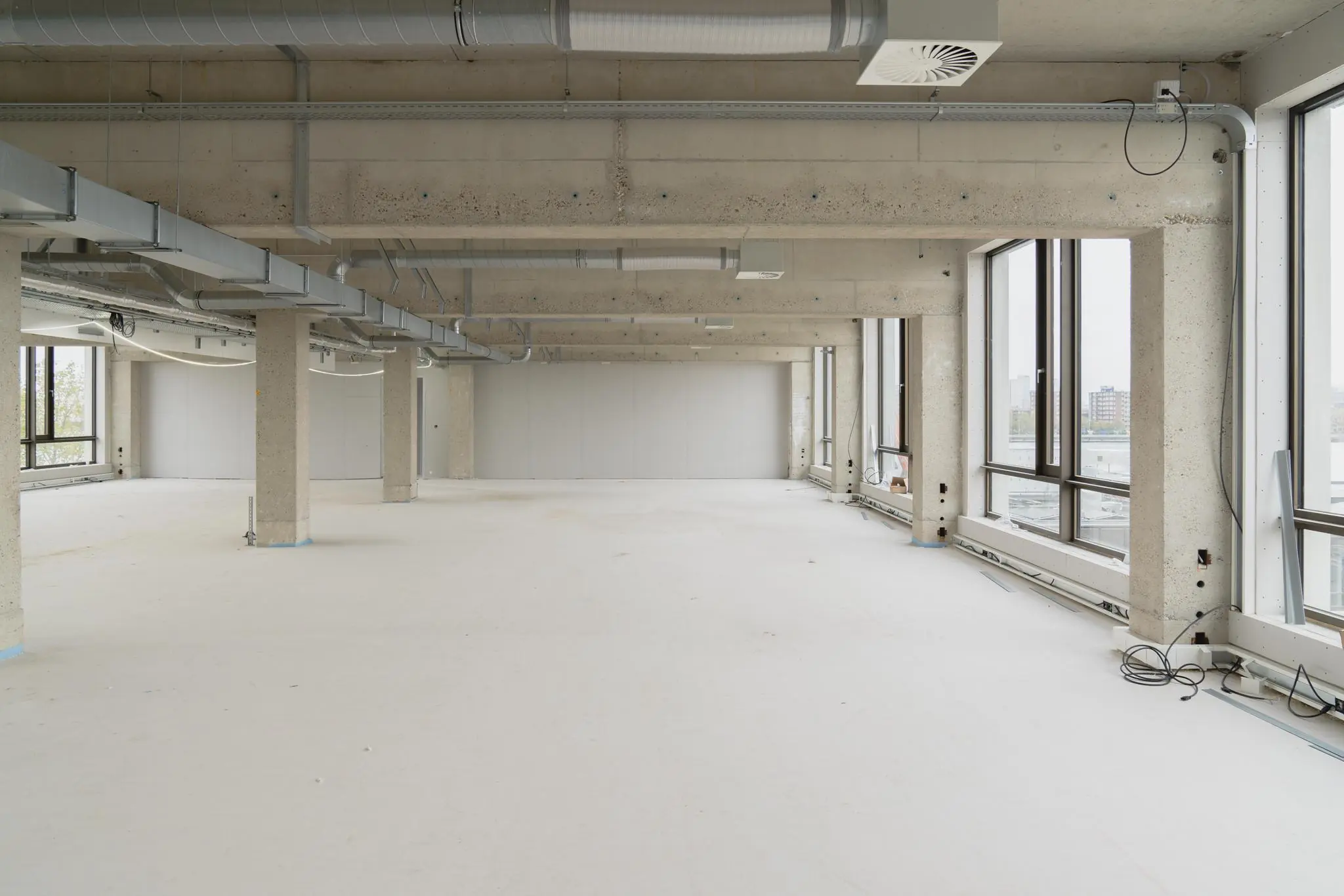 Leeg kantoorpand aan de Sluisjesdijk met betonnen pilaren, grote ramen en zichtbare ventilatiebuizen.