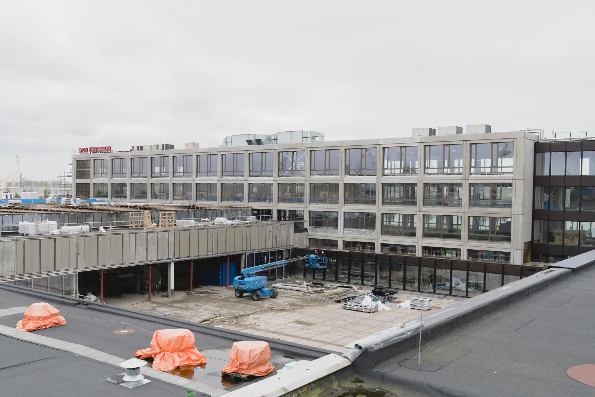 Bouwplaats van een modern gebouw aan de Sluisjesdijk met bouwmaterialen en een hoogwerker op de binnenplaats.