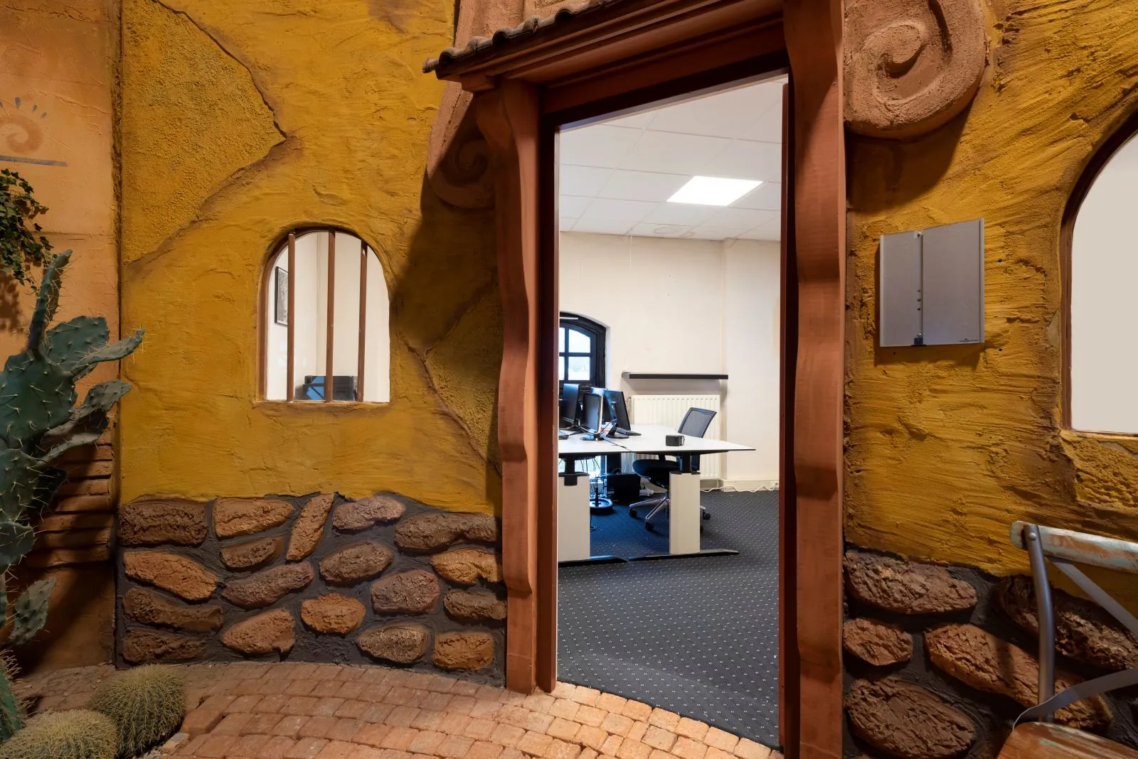 Kantoorruimte met bureaus en computers, gezien door een kleurrijke, zuidwesters gethematiseerde ingang met steen- en stucwerk.