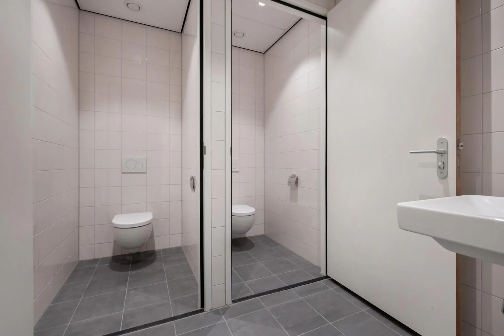 Moderne toiletruimte met zwevend toilet, witte wandtegels en grijze vloertegels aan de Saturnusstraat.