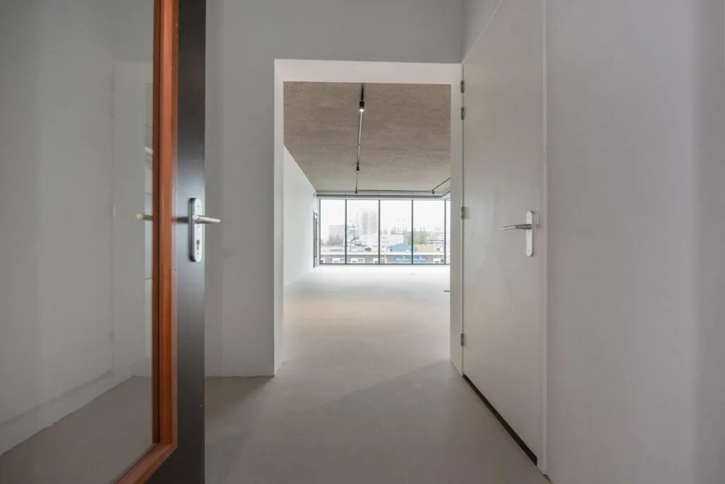 Doorkijk vanuit een gang naar een lichte, lege ruimte met grote ramen aan de Saturnusstraat.