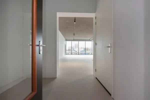 Doorkijk vanuit een gang naar een lichte, lege ruimte met grote ramen aan de Saturnusstraat.