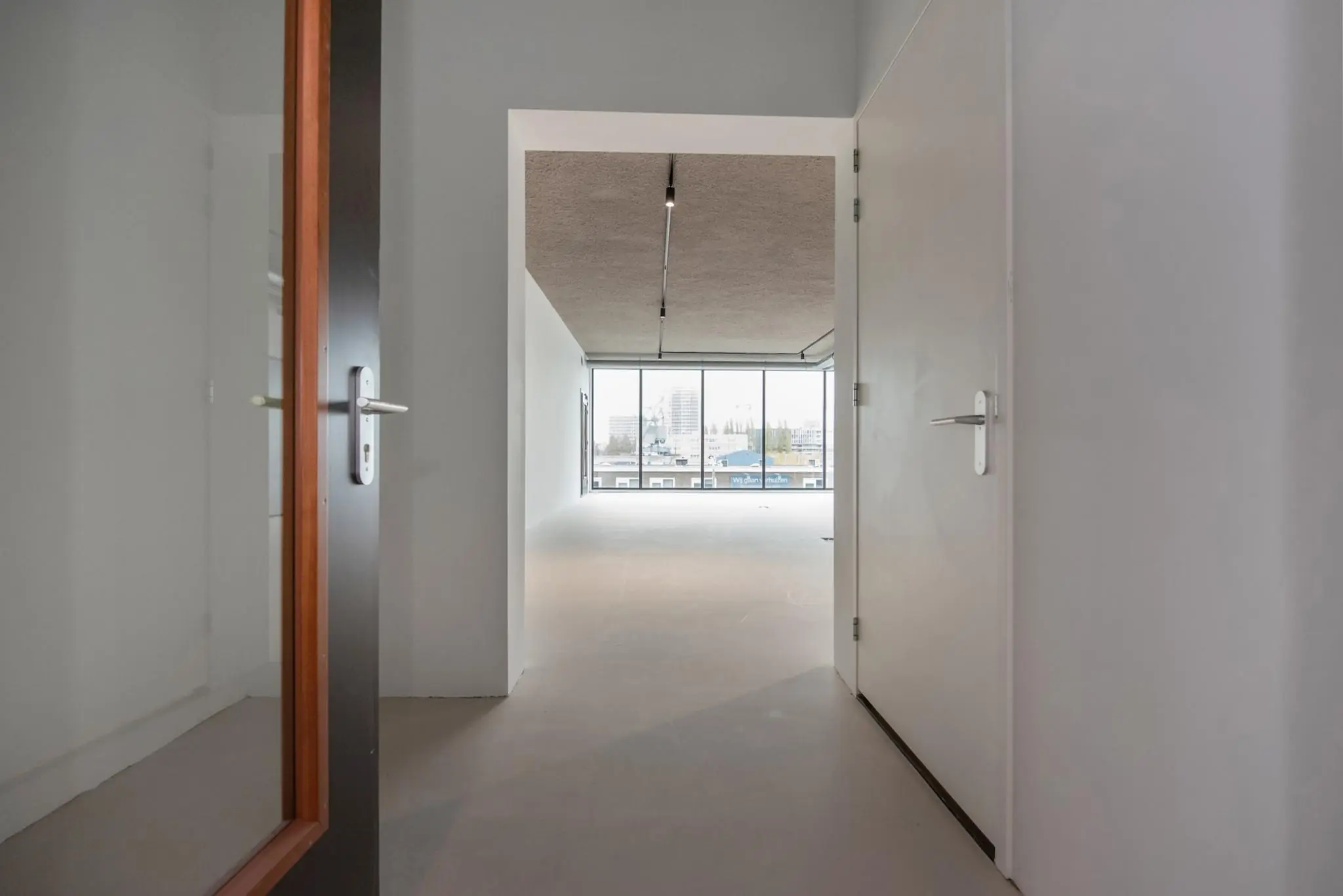 Doorkijk vanuit een gang naar een lichte, lege ruimte met grote ramen aan de Saturnusstraat.