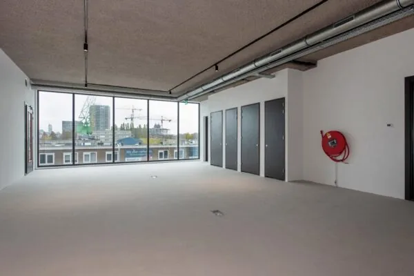 Leeg kantoorpand aan de Saturnusstraat met grote ramen, zicht op bouwkranen en meerdere zwarte deuren.