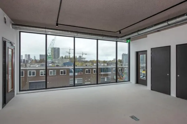 Lichte, lege kantoorruimte aan de Saturnusstraat met groot raam en uitzicht op een stedelijk bouwproject.