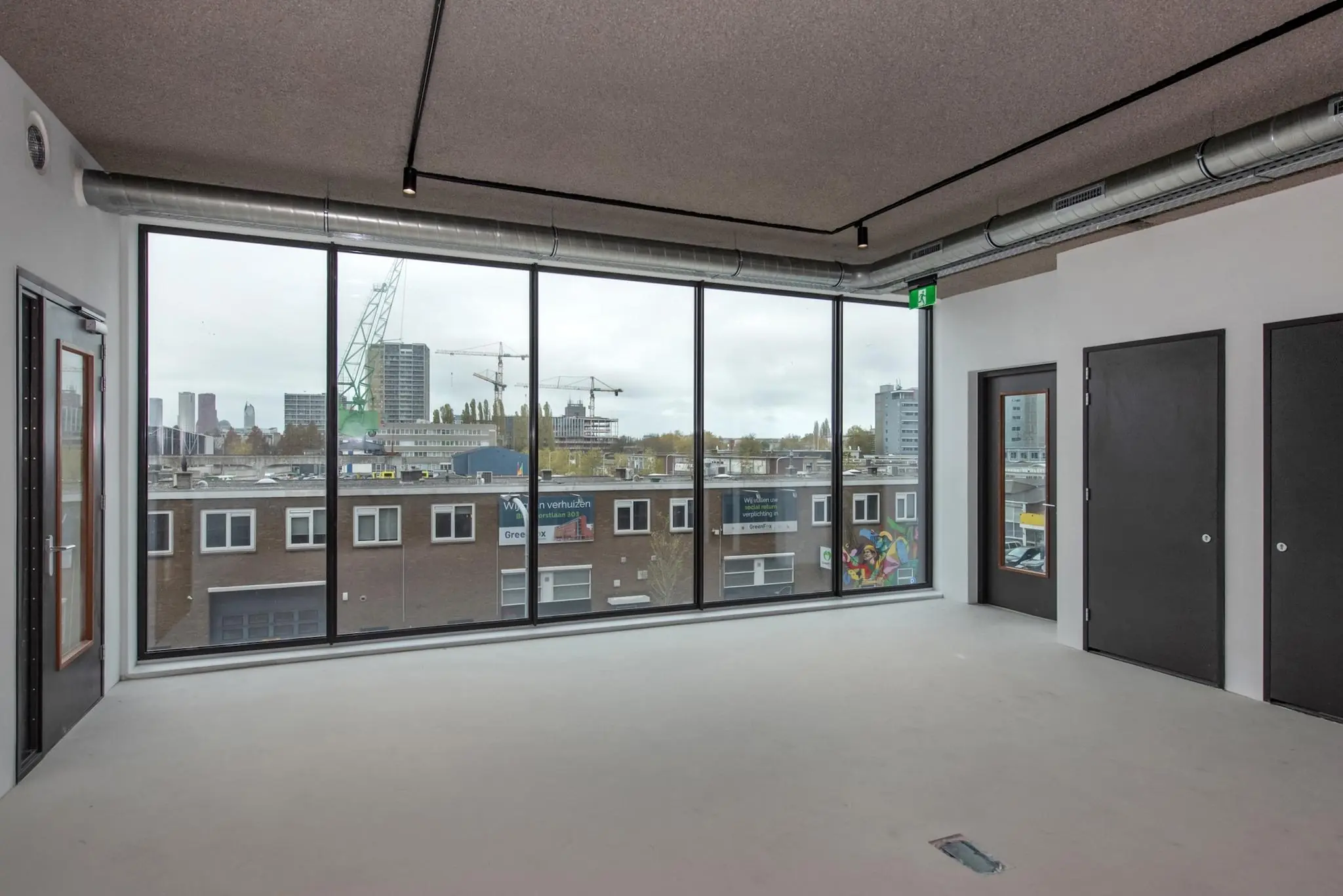 Lichte, lege kantoorruimte aan de Saturnusstraat met groot raam en uitzicht op een stedelijk bouwproject.
