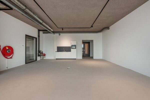 Lege bedrijfsruimte aan de Saturnusstraat met een kitchenette, betonnen vloer en zichtbare plafondleidingen.