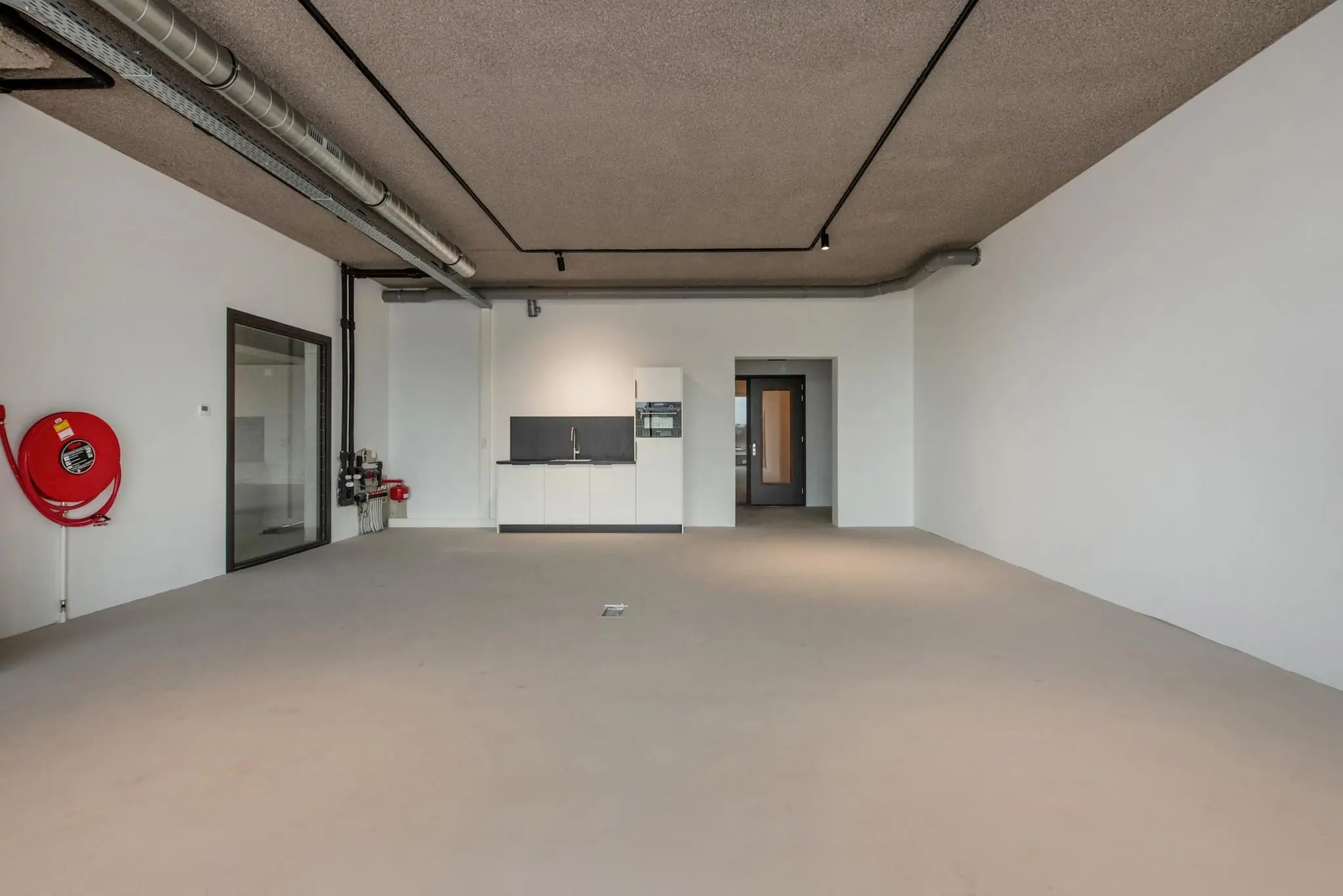 Lege bedrijfsruimte aan de Saturnusstraat met een kitchenette, betonnen vloer en zichtbare plafondleidingen.