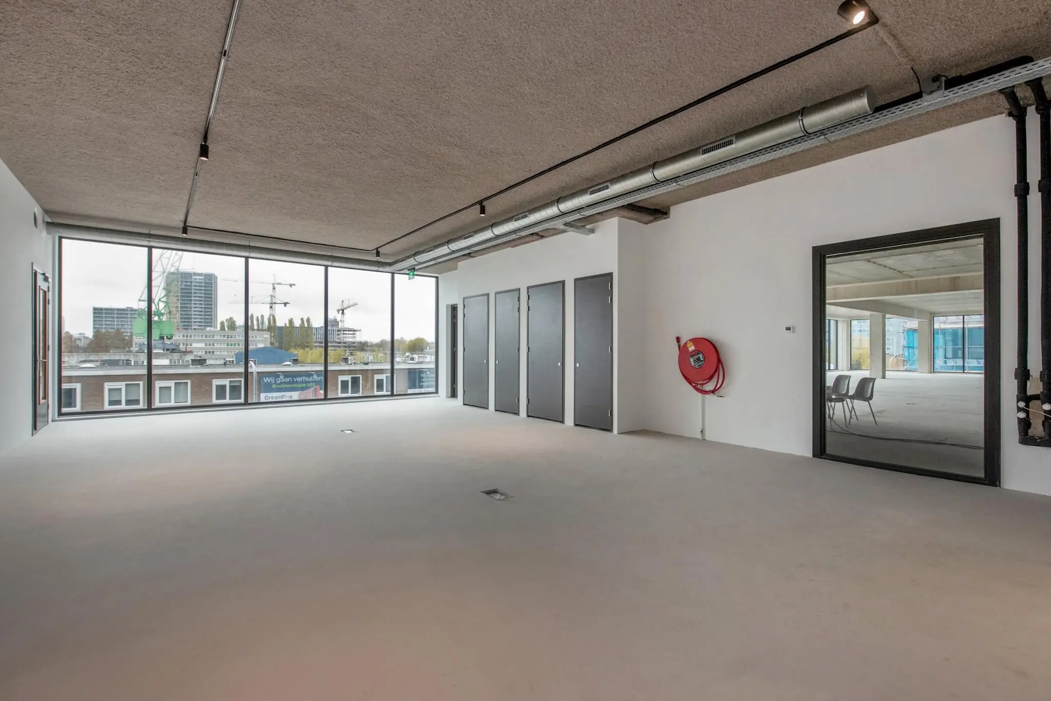 Leeg kantoorpand aan de Saturnusstraat met grote ramen, betonnen vloer en zicht op de stad.