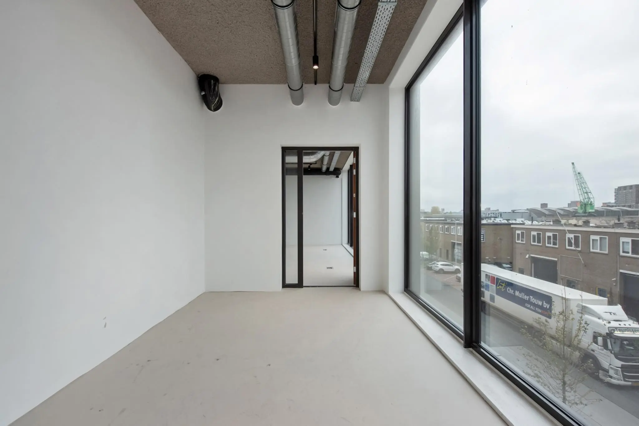 Leeg kantoorpand aan de Saturnusstraat met grote ramen en uitzicht op een industrieel bedrijfsgebouw en vrachtverkeer.