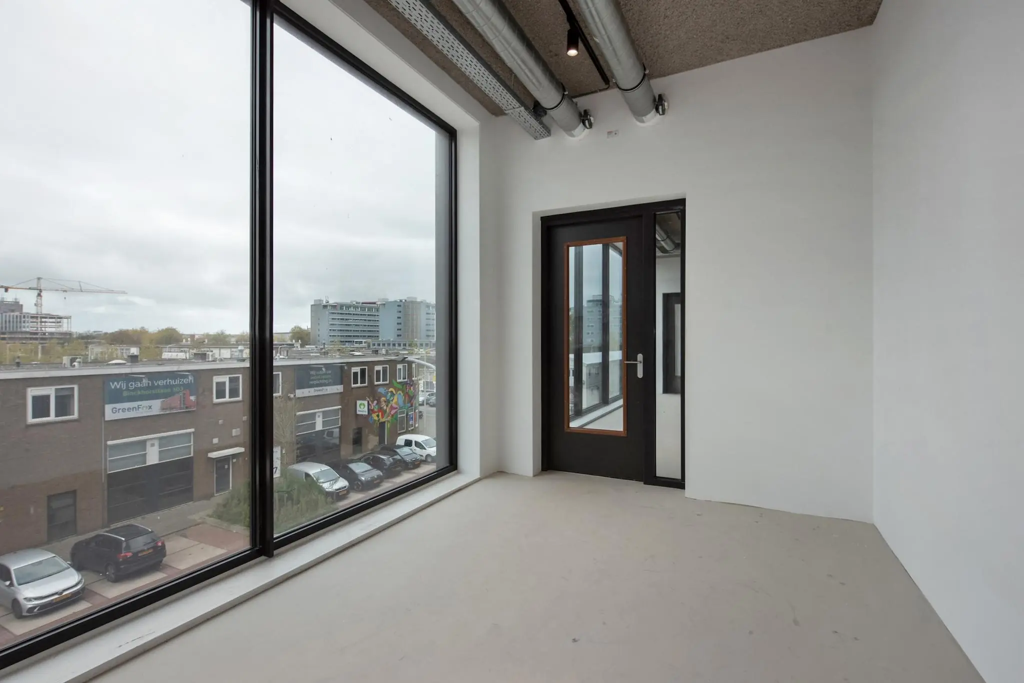 Leeg kantoorruimte met groot raam en uitzicht op de Saturnusstraat in een stedelijke omgeving.