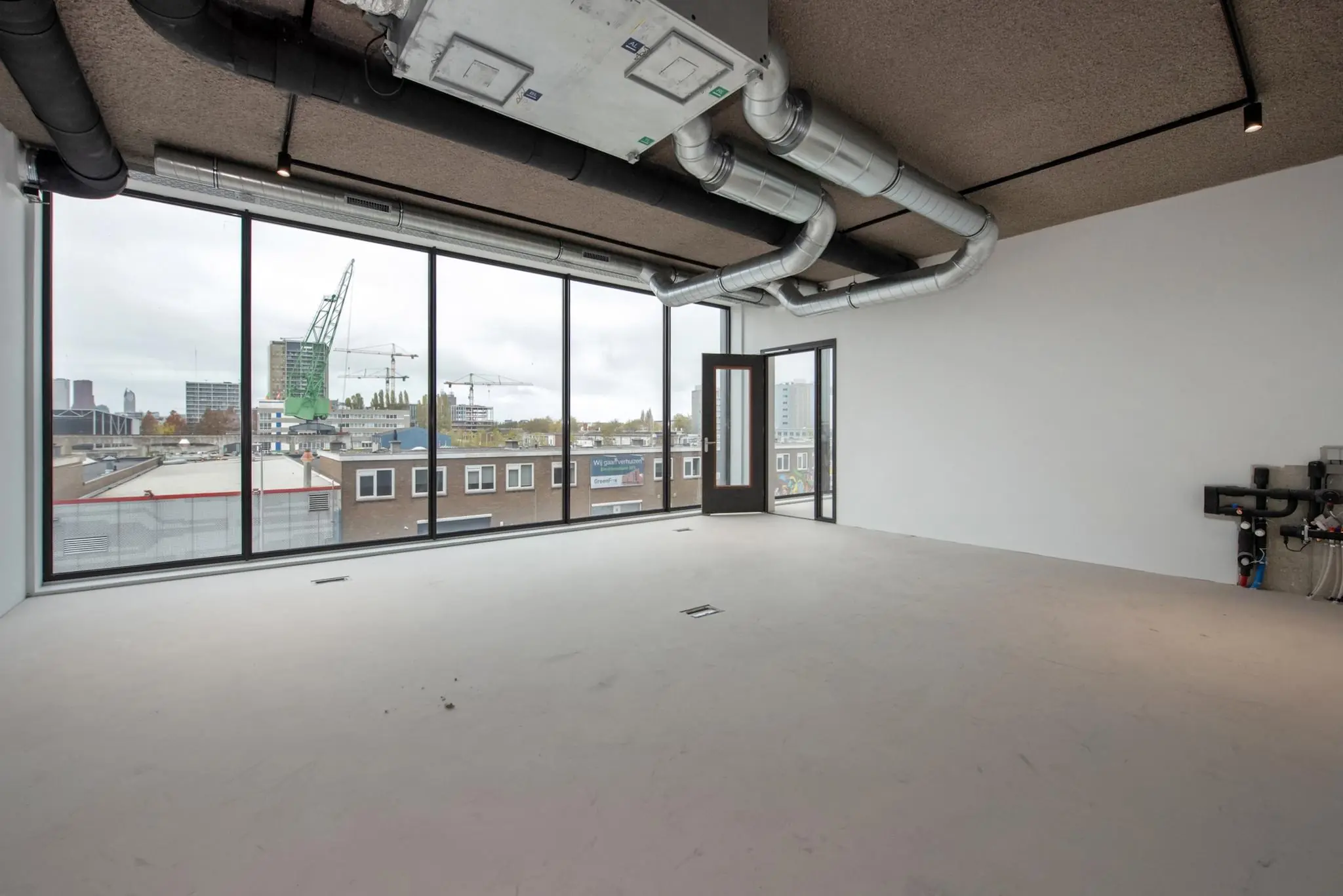 Leeg industrieel kantoorpand aan de Saturnusstraat met grote ramen en zicht op de stad en bouwkranen.