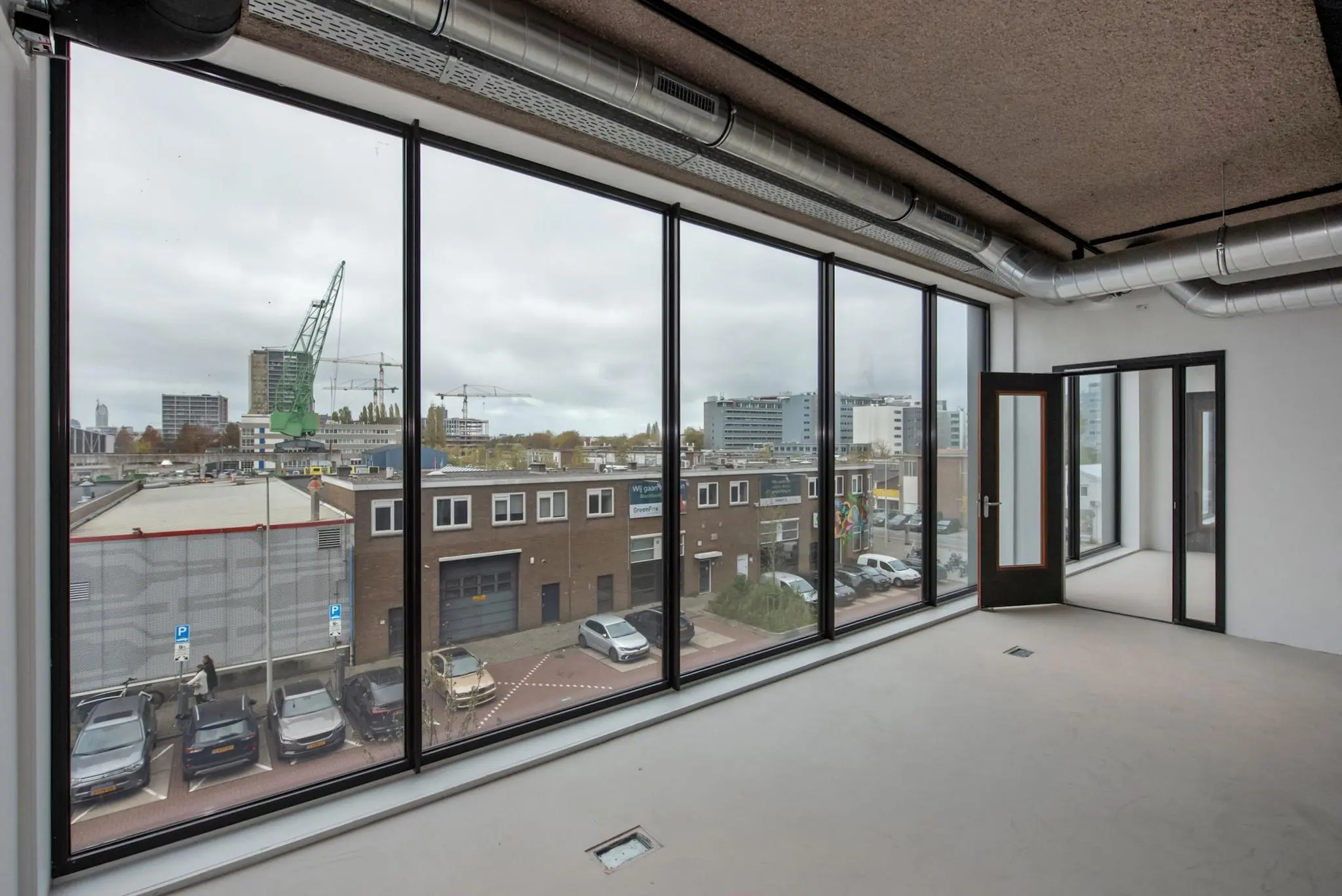 Leeg kantoorpand aan de Saturnusstraat met grote ramen en uitzicht op een bedrijventerrein en hijskranen.