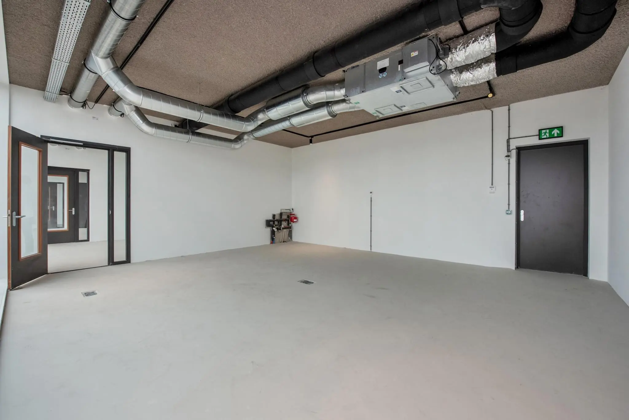 Leeg industrieel kantoor- of bedrijfsruimte aan de Saturnusstraat met zichtbare ventilatiebuizen en witte muren.