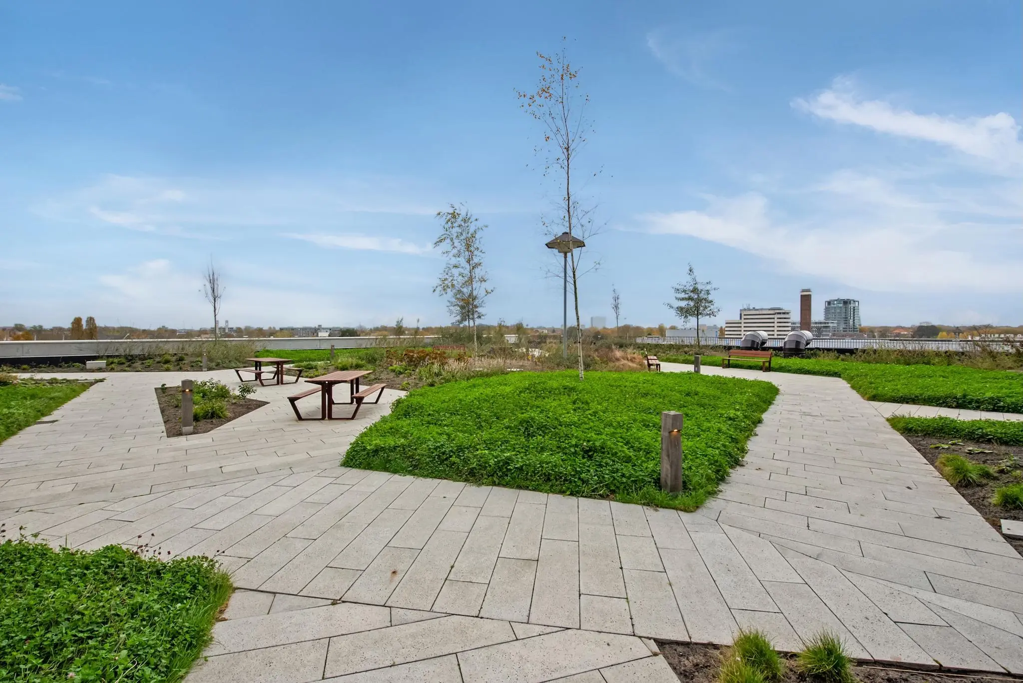 Moderne daktuin met betegelde paden, picknicktafels en uitzicht op de gebouwen aan de Saturnusstraat.