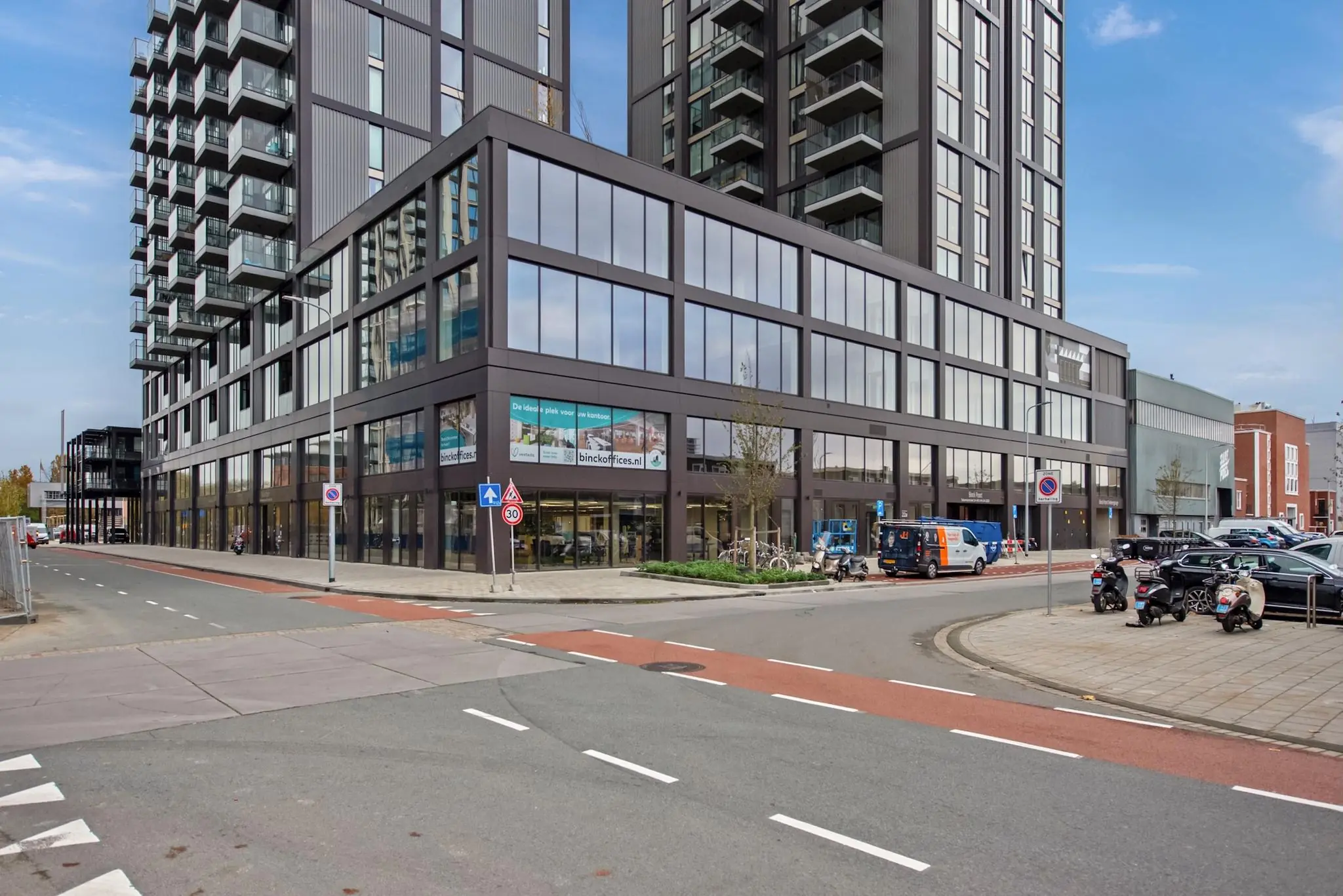Modern kantoorgebouw aan de Saturnusstraat met grote ramen, een fietsenstalling en geparkeerde voertuigen op de voorgrond.